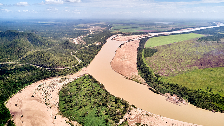 A long-spanning river leads toward the ocean. It is surrounded by greenery.