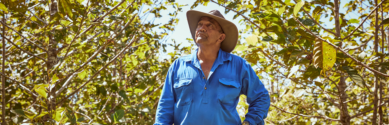 A landholder in a bright blue button-up shirt and tan wide-brimmed hat admires the surrounding greenery of a project site in Queensland.