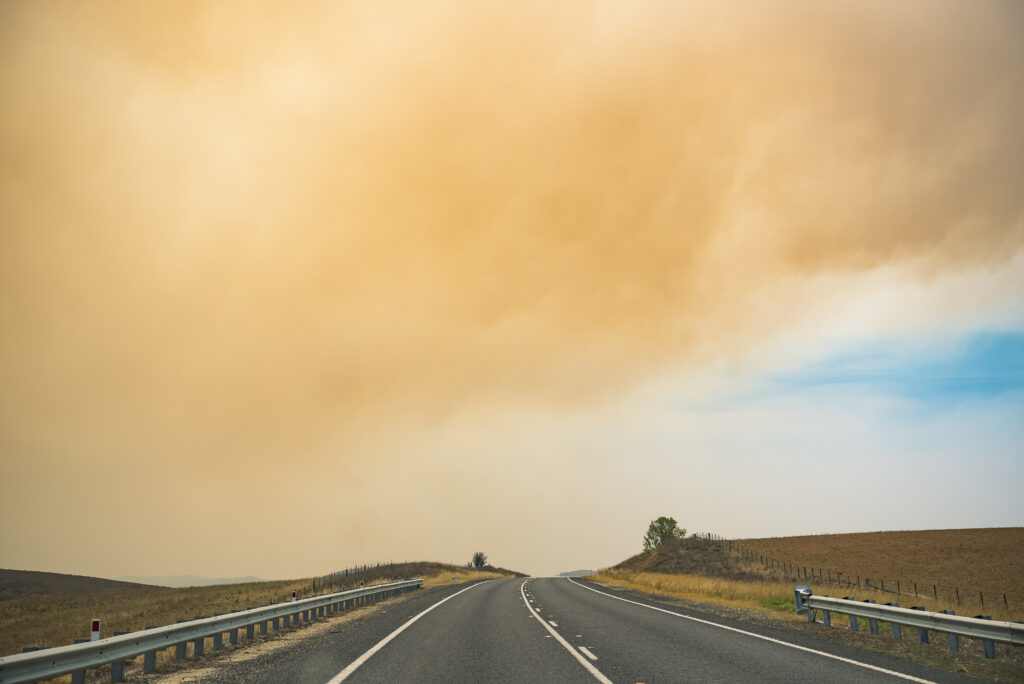 Grey smoke rolls through the orange and blyue sky over a dark grey asphalt road in NSW.