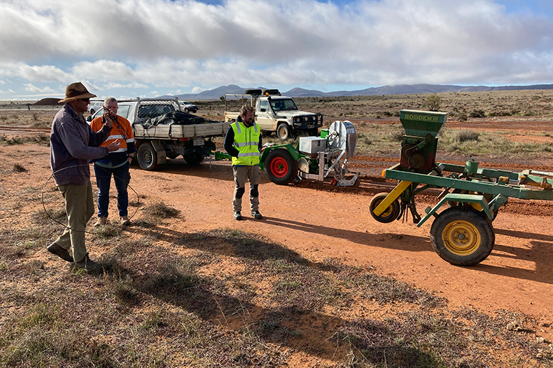 A group of landholders stand around a direct seeder in a dry paddock.
