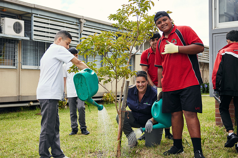 Greening Australia staff member and students water a tree they've just planted.