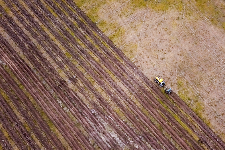 An aerial image of a tractor pulling a direct seeder. On the left of the tractor, two-thirds of the image shows seeded rows, while a third of the image to the right of the tractor shows land yet to be seeded.