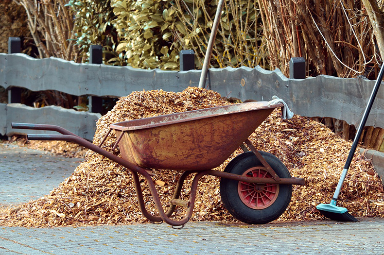 A wheelbarrow stands beside a large pile of mulch.