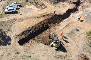 An aerial view of an eroding gully that is being reshaped by a dozer. Utility vehicles and people dressed in high vis can also be seen watching the works in progress.