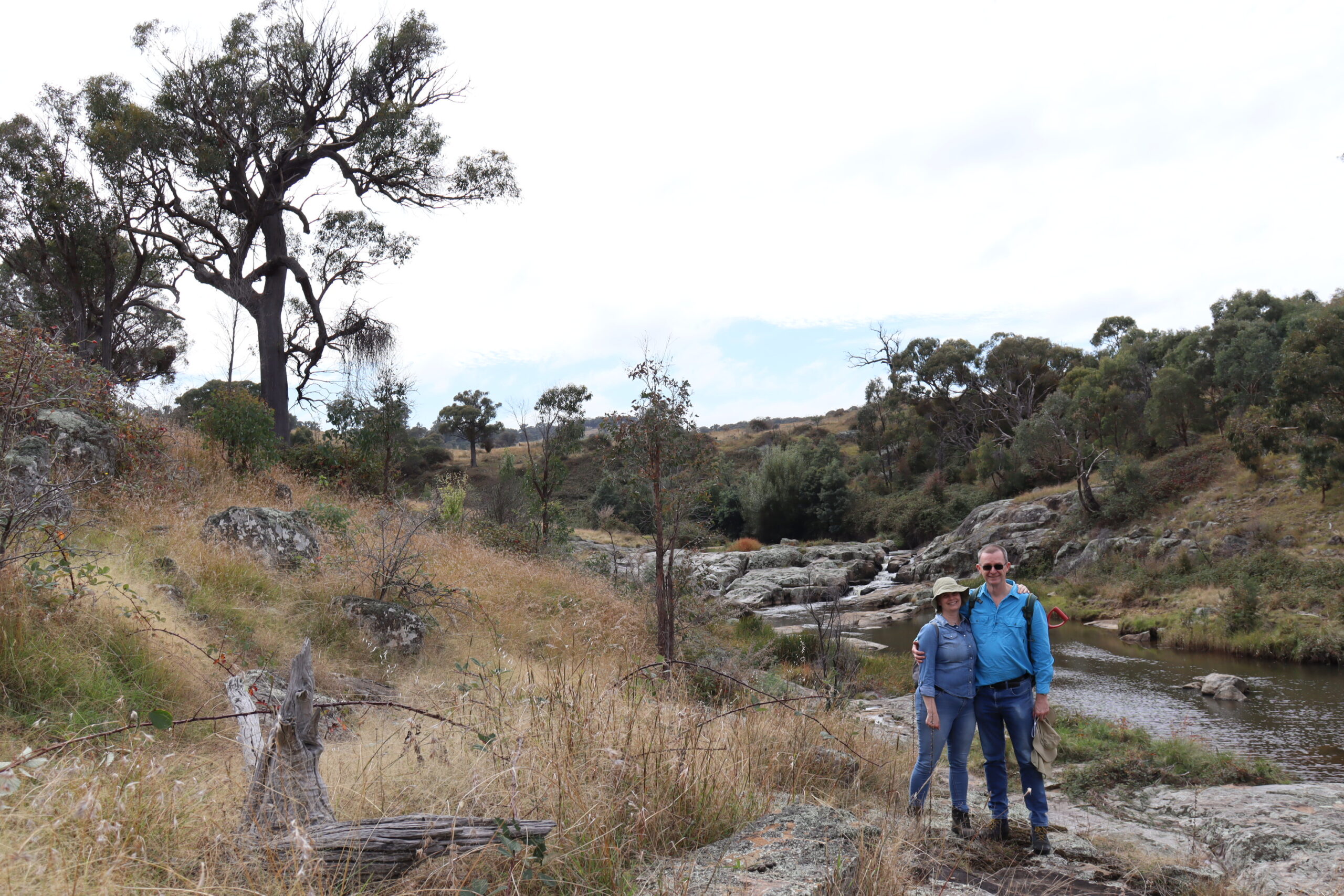 Two people stand by a river on a rock