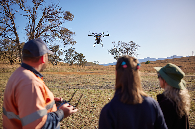A group of people outdoors watch a large drone in the distance.