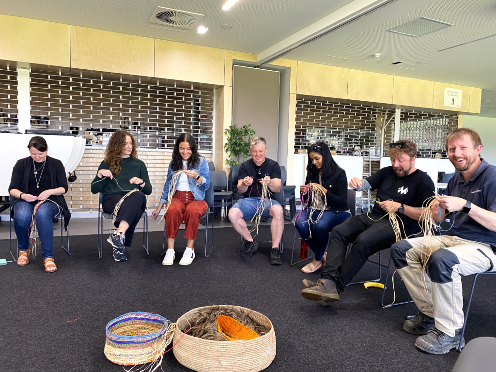 A group of people sit in a circle in an office space weaving
